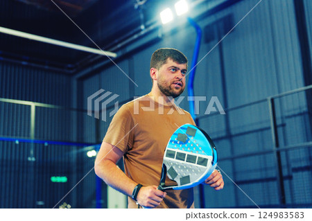 Man prepares to play indoors at a modern sports facility, holding a paddle ready for action during a training session Man prepares to play indoors at a modern sports facility, holding a paddle ready for action during a training session 124983583