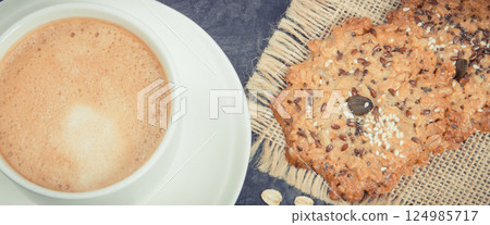Cup of coffee with milk and fresh baked oatmeal cookies on plate. Delicious crunchy dessert Cup of coffee with milk and fresh baked oatmeal cookies on plate. Delicious crunchy dessert 124985717