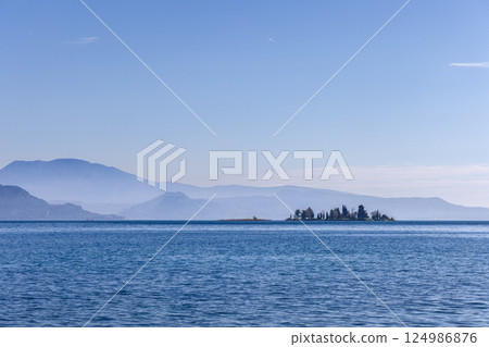 Lake Garda in northern Italy with small San Biagio island visible in soft morning blue haze Lake Garda in northern Italy with small San Biagio island visible in soft morning blue haze 124986876
