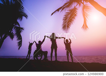 Disabled man in a wheelchair with his family on the beach. Silhouettes at sunset Disabled man in a wheelchair with his family on the beach. Silhouettes at sunset 124986900
