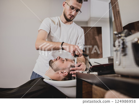 Young man with trendy haircut at barber shop. Barber washes customer head. Young man with trendy haircut at barber shop. Barber washes customer head. 124986958