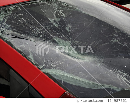 Shattered and broken windshield on a bright red car showcasing the damage to its glass surface 124987861