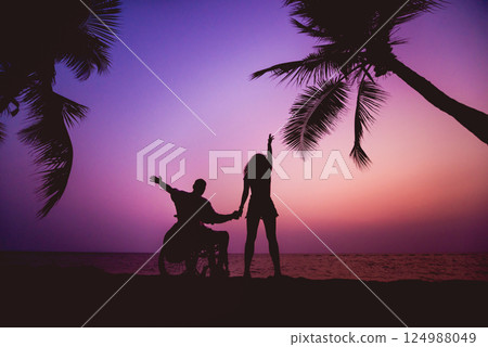Disabled man in a wheelchair with his wife on the beach. Silhouettes at sunset Disabled man in a wheelchair with his wife on the beach. Silhouettes at sunset 124988049
