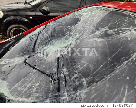 Shattered and broken windshield on a bright red car showcasing the damage to its glass surface Shattered and broken windshield on a bright red car showcasing the damage to its glass surface 124988057