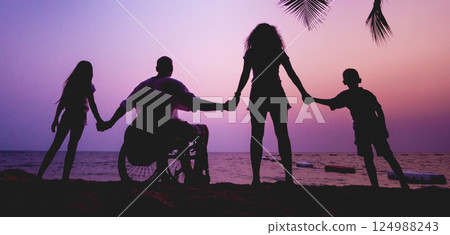 Disabled man in a wheelchair with his family on the beach. Silhouettes at sunset Disabled man in a wheelchair with his family on the beach. Silhouettes at sunset 124988243