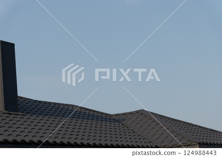 High-quality tiled roof covers a house, reflecting skilled craftsmanship in construction on a bright sunny day with a clear blue sky High-quality tiled roof covers a house, reflecting skilled craftsmanship in construction on a bright sunny day with a clear blue sky 124988443