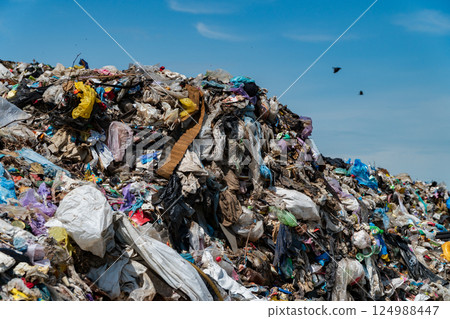 A vast, towering pile of mixed debris and plastic waste fills an urban landfill under a clear blue sky, illustrating a pressing environmental crisis A vast, towering pile of mixed debris and plastic waste fills an urban landfill under a clear blue sky, illustrating a pressing environmental crisis 124988447
