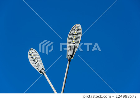 Two contemporary street lights illuminate the area under a vibrant blue sky, showcasing their sleek design and functionality 124988572