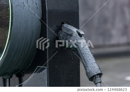 Water droplets cling to a charging gun as it fits into an electric vehicle's charging port at a modern station in the city 124988623