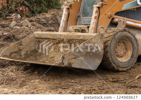 A skid steer loader is actively moving dirt and debris at a construction site on a cloudy day, showcasing the work in progress A skid steer loader is actively moving dirt and debris at a construction site on a cloudy day, showcasing the work in progress 124988627