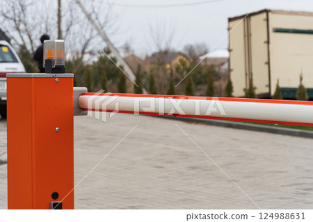 A parking lot barrier arm stands upright with a warning light on top, surrounded by vehicles and trees on a gray day A parking lot barrier arm stands upright with a warning light on top, surrounded by vehicles and trees on a gray day 124988631