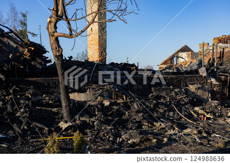 Charred remains of structures and trees illustrate the devastation caused by a recent wildfire in a rural setting, with clear skies above Charred remains of structures and trees illustrate the devastation caused by a recent wildfire in a rural setting, with clear skies above 124988636