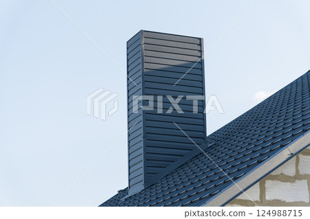 A sleek chimney extends upward from a contemporary home, framed by a clear blue sky and bright afternoon sunlight illuminating the tidy roof A sleek chimney extends upward from a contemporary home, framed by a clear blue sky and bright afternoon sunlight illuminating the tidy roof 124988715