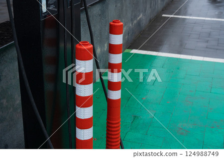 Barriers painted in red and white mark the location of an electric vehicle charging station on a slick green pavement in an urban setting Barriers painted in red and white mark the location of an electric vehicle charging station on a slick green pavement in an urban setting 124988749