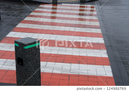 A crosswalk features vibrant red and white stripes, contrasting against wet pavement, while a decorative pole marks the area in a city 124988769