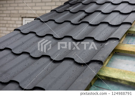 Freshly installed black roofing panels glisten with rainwater, showcasing their sleek design and durability against the elements Freshly installed black roofing panels glisten with rainwater, showcasing their sleek design and durability against the elements 124988791