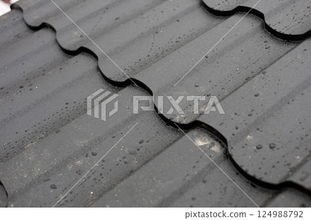 Dark roof tiles are covered with droplets of rainwater after a light rain in a city during the afternoon, showcasing the weather effects on roofing Dark roof tiles are covered with droplets of rainwater after a light rain in a city during the afternoon, showcasing the weather effects on roofing 124988792