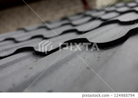 Water droplets rest on a textured metal roofing surface, showcasing its curved design and shiny finish after a recent rain shower Water droplets rest on a textured metal roofing surface, showcasing its curved design and shiny finish after a recent rain shower 124988794