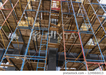 Workers utilize colorful scaffolding to access upper levels of a building under renovation in an urban area during daylight 124988813