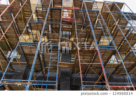 Workers utilize scaffolding to renovate a multi-story building in an urban area under clear skies, showcasing construction progress 124988814