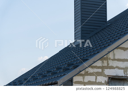 A detailed view of a recently completed metal roof on a contemporary house, highlighting the chimney and smooth lines against the sky A detailed view of a recently completed metal roof on a contemporary house, highlighting the chimney and smooth lines against the sky 124988825