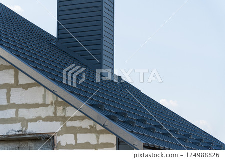 A detailed view of a recently installed metal roof on a house emphasizing the chimney and surrounding construction elements A detailed view of a recently installed metal roof on a house emphasizing the chimney and surrounding construction elements 124988826