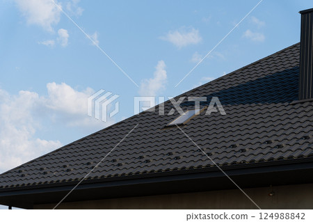 Bright midday sky highlights the dark shingles of a modern house roof that includes a skylight, surrounded by soft clouds Bright midday sky highlights the dark shingles of a modern house roof that includes a skylight, surrounded by soft clouds 124988842