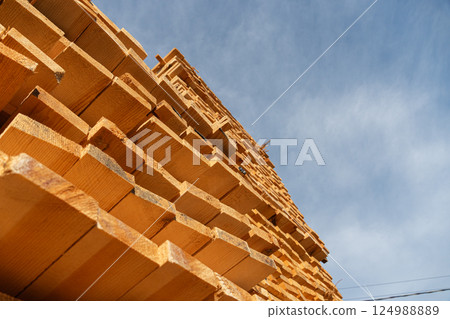 Tall stacks of lumber stretch skyward against a backdrop of clear blue, showcasing the beauty of natural wood and craftsmanship Tall stacks of lumber stretch skyward against a backdrop of clear blue, showcasing the beauty of natural wood and craftsmanship 124988889