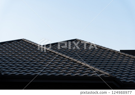 Black tile roof with a wave-like design stands against a clear blue sky in a suburban area, showcasing modern home architecture Black tile roof with a wave-like design stands against a clear blue sky in a suburban area, showcasing modern home architecture 124988977