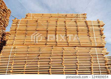 Tall stacks of fresh lumber are neatly arranged at a construction site against a bright sky, ready for upcoming building projects 124989054
