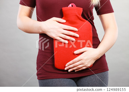 Girl having stomach ache, holding hot water bottle 124989155