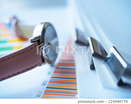 Graphs, documents, and a wristwatch on the table 124990776
