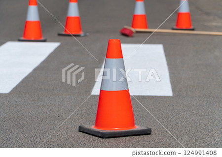Bright orange traffic cones standing on asphalt. Painting road markings. Traffic cones for road works 124991408