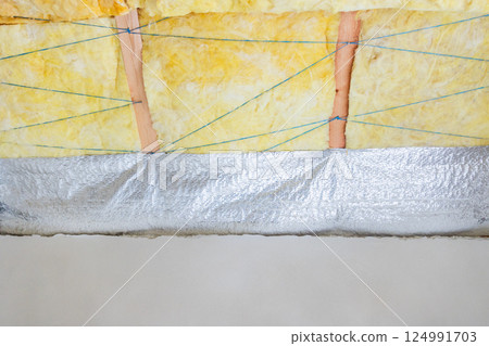 Yellow glass wool insulation held by strings and covered with vapor barrier during renovation work 124991703