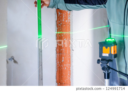 Construction worker using laser level and ruler taking measurements on site Construction worker using laser level and ruler taking measurements on site 124991714