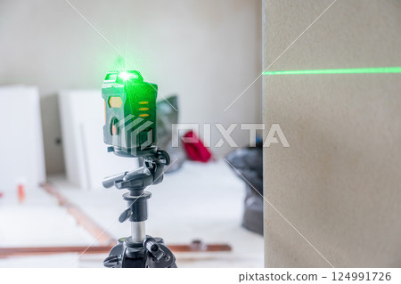 Cross line laser level tool projecting green beam in empty room 124991726