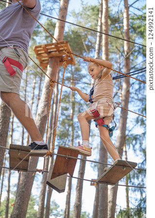A little girl and her dad walk a rope track in an amusement park A little girl and her dad walk a rope track in an amusement park 124992141