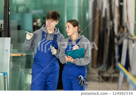 Young guy and woman with folder discuss work at glass factory Young guy and woman with folder discuss work at glass factory 124992534