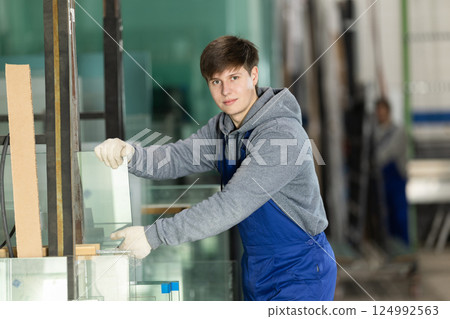 Young guy stacking glass sheets in factory 124992563