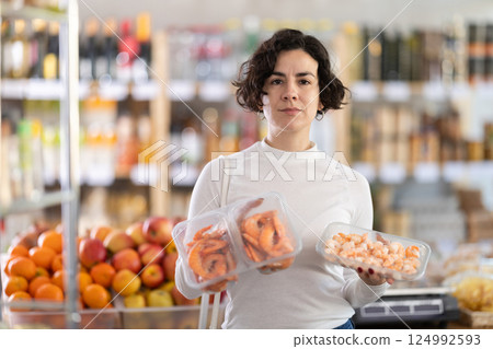 Adult woman chooses prawns in grocery store Adult woman chooses prawns in grocery store 124992593