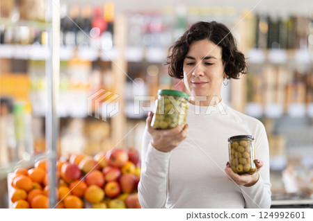 In store, woman near counter are looking at pickled green olives jar In store, woman near counter are looking at pickled green olives jar 124992601
