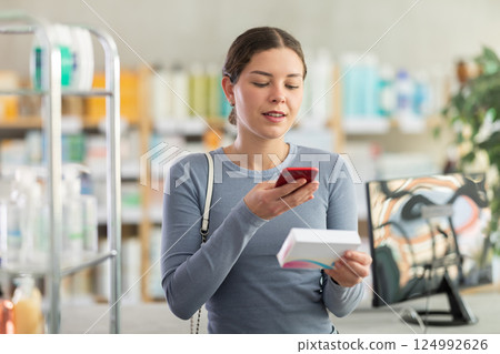 Young girl customer scanning QR-code on pills box 124992626