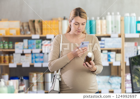 Pregnant woman scanning barcode on choosing syrup in drugstore 124992697
