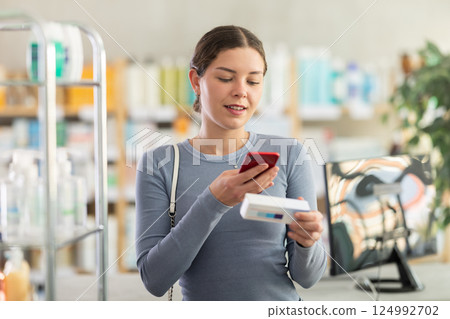 Female customer scanning QR code on box of ointment in pharmacy 124992702
