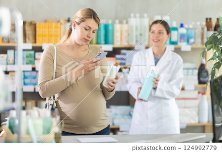 Pregnant woman in pharmacy scans QR code on shampoo, pharmacist offer similar product in background Pregnant woman in pharmacy scans QR code on shampoo, pharmacist offer similar product in background 124992779