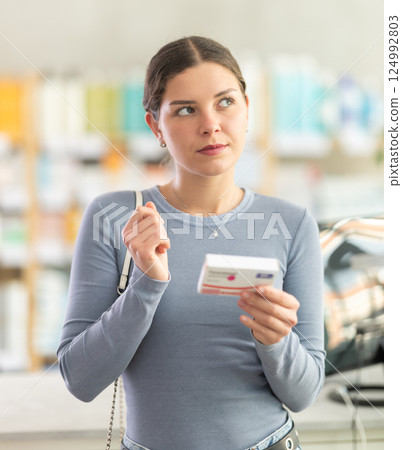 Young woman choosing pain or fever relief medicine in pharmacy 124992803