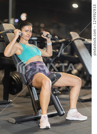 During training session in mini group of athletes, woman exercises on shoulder press machine During training session in mini group of athletes, woman exercises on shoulder press machine 124992918