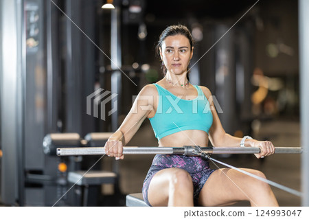 In gym, woman uses cable row machine to strengthen arm muscles In gym, woman uses cable row machine to strengthen arm muscles 124993047