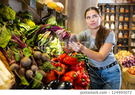 Woman diligently picking out beets to buy in vegetable aisle of supermarket 124993072