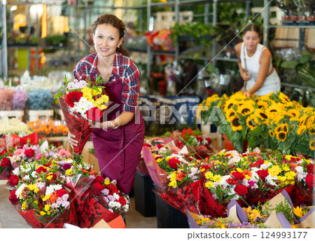 Positive female seller in apron holds designer bouquet in hands 124993177